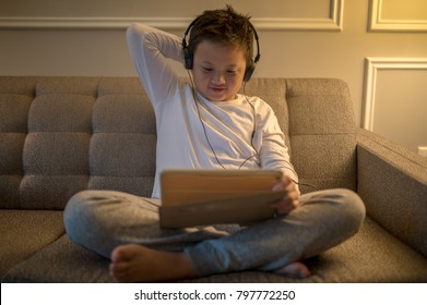 Asian Gen Z Boy Enjoys Watching Tablet With Headphone, Put Right Hand Scratch Head