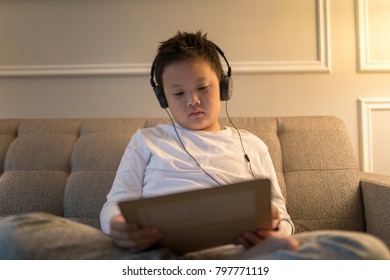 Asian Gen Z Boy Listen To Music From Headphone Connected To Tablet In Hotel Room