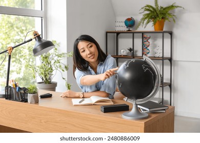 Asian Geography teacher with globe sitting at table in classroom - Powered by Shutterstock