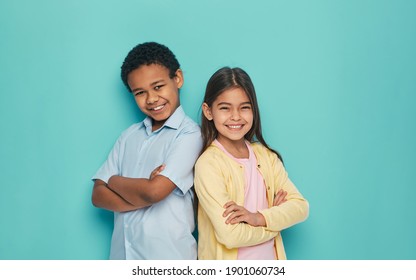 Asian Girl And African American Boy Standing Back To Back With Arms Crossed On A Turquoise Background