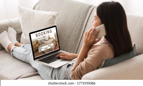 Asian Girl Booking Hotel Online, Talking On Phone With Reservation Team, Sitting On Couch At Home At Using Laptop