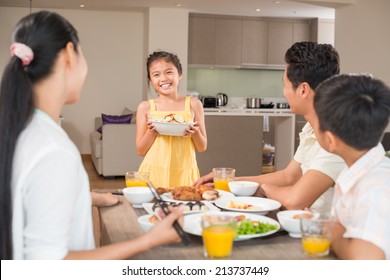 Asian Girl With A Bowl Of Salad Standing In Front Of Family Dinner Table