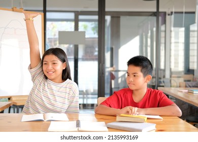 asiatische Mädchenschülerin, die im Klassenzimmer lernt, die Hand zu heben. Schulbildung