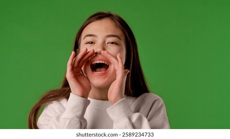 Asian girl child holds hands around mouth and screaming shouting, positive expression, isolated on chroma key green screen studio background mockup.
