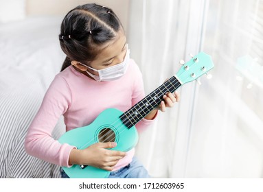 Asian Girl Child Hygienic Mask Stay Isolation At Home For Self Quarantine For Protect Against Virus COVID-19,Little Girls During Detention Looking For Activities Learn More About Playing The Ukulele.