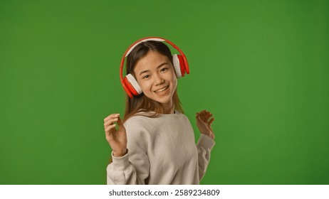 Asian girl child listening music in headphones singing and dancing, positive expression, isolated on chroma key green screen studio background mockup.