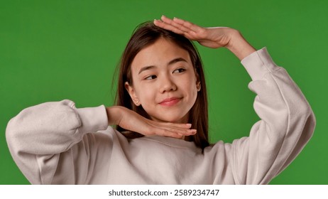 Asian girl child posing at camera like a model, touching face and makes cool poses, positive expression, isolated on chroma key green screen studio background mockup.