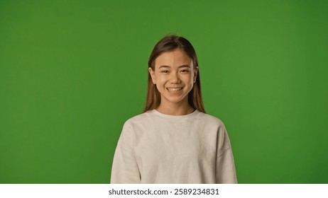 Asian girl child in shirt standing looking at camera and smiling, positive expression, isolated on chroma key green screen studio background mockup.