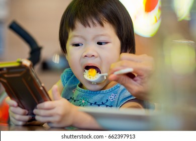 asian girl child typing  smartphone and eating food - Powered by Shutterstock