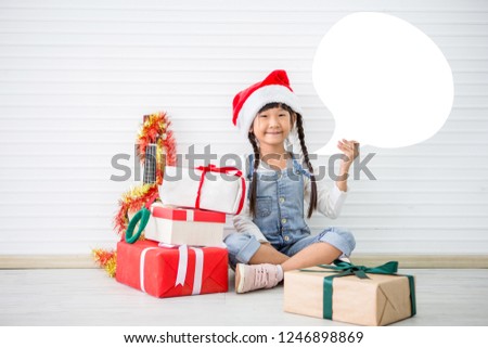 asian girl in Christmas Santa hat show gift box with pile of presents and Ukulele on white background . Chinese childen celebrating happy new year. kid smiling with sketch speech bubble copy space