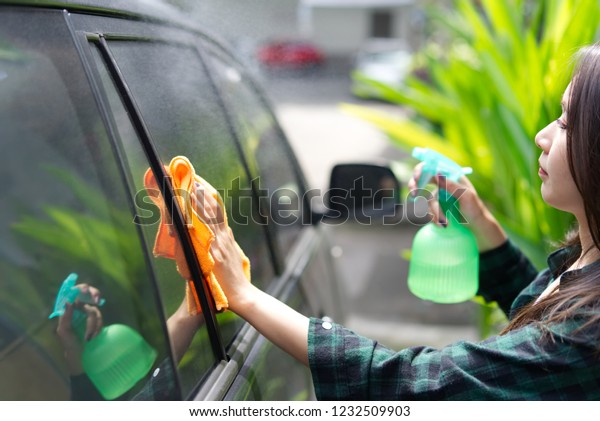 Asian girl\
cleaning the car window by using car wipe cloth and spraying the\
cleaning liquid. Car cleaning\
concept.