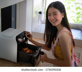 Asian Girl Cooking A Fried Chicken By Air Fryer Machine In Her Kitchen At Home