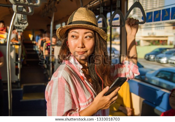 Asian girl with earphone standing on the bus\
enjoying the trip.