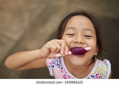 Asian Girl Eating Ice Cream In Outdoor. Filipina Kid Eating An Ice Cream And Staring At Camera.