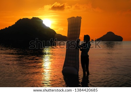 Asian girl enjoying with inflatable raft on the beach at sunset, Red sky background at Archipelago island in Thailand.