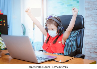 Asian Girl Feel Happy With Online Education. Littel Girl Wear Medical Mask Studying At Home, Working At Laptop Notebook With Special Teacher Exercise In Coronavirus Quarantine.