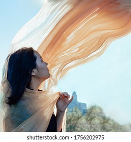 Asian Girl With A Flying Orange Scarf Against A Blue Sky