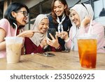 Asian girl friends from Indonesia sitting in cafe using mobile phone together to share content on social media