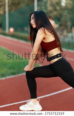 Asian girl go in for sports on a sports track on the street. Red treadmill. Girl with headphones. Girl in a sports top and leggings.