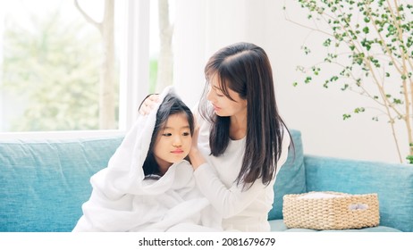 Asian girl having her mother wipe her hair with a bath towel.