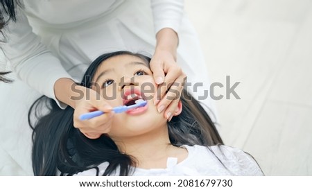 Asian girl having mom brush her teeth. Dental care. Oral care.