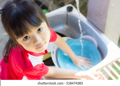 Asian girl help parents work , she wash the dish happily.