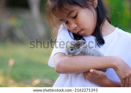Asian girl holding adorable bunny fluffy in hand with tenderness and love. People take care and play with a pet.