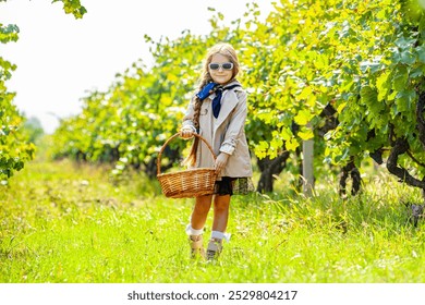 An Asian girl holds a grape and a box of grapes in her hand. Children working inside a vineyard in the background of green vineyards. The child was wearing a plaid shirt and a smiling hat. Grape farm - Powered by Shutterstock