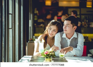 Asian girl hugging her boyfriend in a restaurant. They are look to outside.