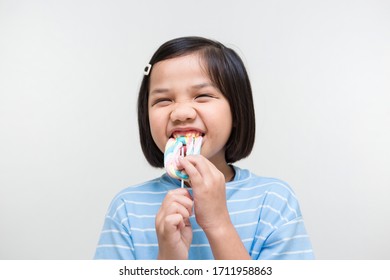 Asian Girl Kid Consuming Sweet Candy Lollipop With Sugar Added, Causing Loss Teeth And Unhealthy Oral Care. Funny Portrait Of Girl Eating Sugary Food On White Background.