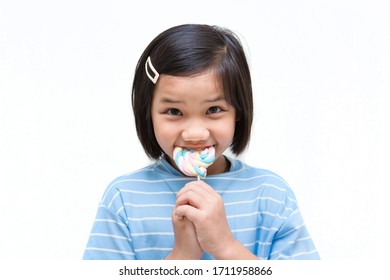 Asian Girl Kid Consuming Sweet Candy Lollipop With Sugar Added, Causing Loss Teeth And Unhealthy Oral Care. Funny Portrait Of Girl Eating Sugary Food On White Background.