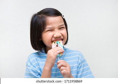 Asian Girl Kid Consuming Sweet Candy Lollipop With Sugar Added, Causing Loss Teeth And Unhealthy Oral Care. Funny Portrait Of Girl Eating Sugary Food On White Background.