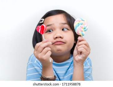 Asian Girl Kid Consuming Sweet Candy Lollipop With Sugar Added, Causing Loss Teeth And Unhealthy Oral Care. Funny Portrait Of Girl Eating Sugary Food On White Background.