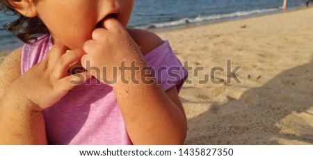 asian girl kids playing sand by the beach while putting fingers in her mouth. family and health concept -image