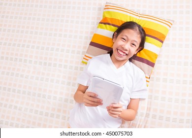 Asian Girl Laying Down, Looking Straight Up At Camera, Using Computer Tablet, Room For Copy Space Text