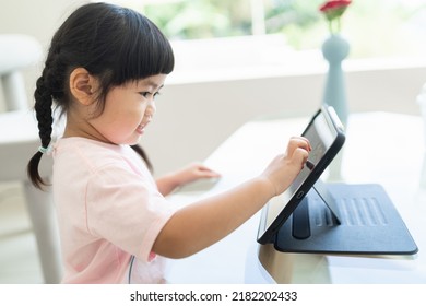 Asian Girl Looking And Touch On Tablet Screen Attentively. Overstimulated Children Concept. Too Much Screen Time. Asian Girl Watching Videos While Tv Is Working.