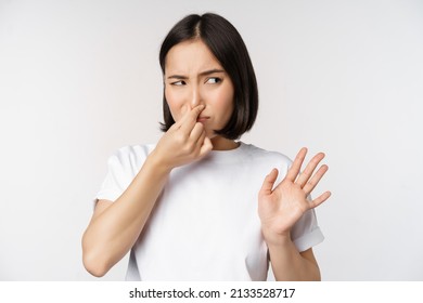 Asian Girl Looks Disgusted, Rejecting Product With Bad Smell, Shut Nose From Aversion And Cringe, Standing Against White Background