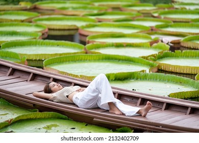 Asian Girl Is Lying Down On The New Vintage Wood Boat On The Lily Lotus Leaf Pond At Outdoor Field.