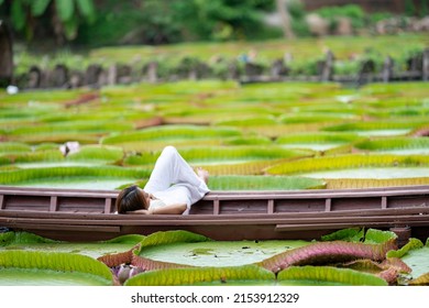 Asian Girl Is Lying Down On The New Vintage Wood Boat On The Lily Lotus Leaf Pond At Outdoor Field.