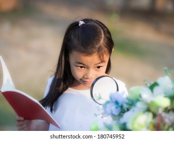 Asian girl with magnifying glass outdoors and note for flower description