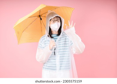 Asian girl makes OK gesture, wears protective mask to reduce breathing pollutants, wears raincoat, hides under umbrella. Air pollution concept - Powered by Shutterstock