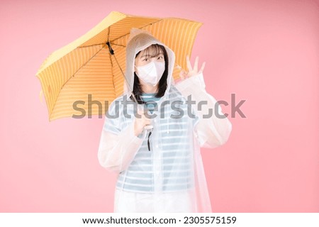 Asian girl makes OK gesture, wears protective mask to reduce breathing pollutants, wears raincoat, hides under umbrella. Air pollution concept