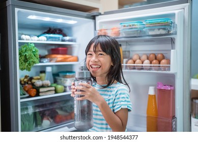 Asian Girl Open Fridge Door Drinking A Bottle Of Water