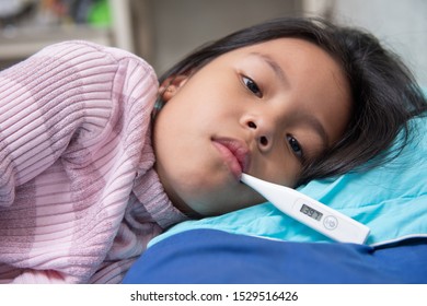 An Asian Girl Is Open Her Eyes, Have A Thermometer In The Mouth. Maybe Have A Cough Until Sore Throat, Difficulty Swallowing, Colds, Flu Or Fever, Should To Meet A Doctor At The Hospital And First Aid