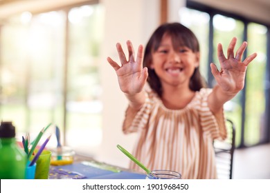 Asian Girl Painting Picture On Table At Home Showing Messy Hands To Camera