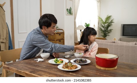 Asian Girl Picky Eater Turning Head And Saying No To Her Dad As He Is Encouraging Her To Take A Bite Of Vegetable. He Holds The Food With Chopsticks Near Her