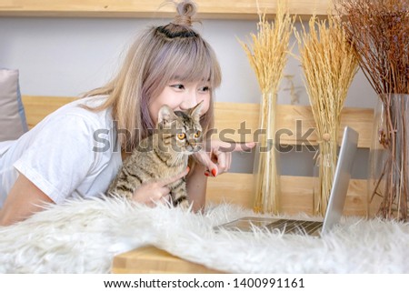 Asian girl playing with cats on the sofa. Female are playful with cats in the living room. A beautiful woman is sitting with a cat looking at her computer in the living room.