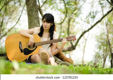 Asian Girl Playing Guitar Under A Tree In The Garden