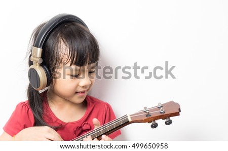 Asian girl is playing Music guitar with headphone on white background. Girl in red shirt is practicing music. little Musician is learning to play acoustic guitar.