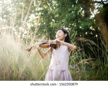 Asian Girl Playing Violin In The Grass With Sun Light.